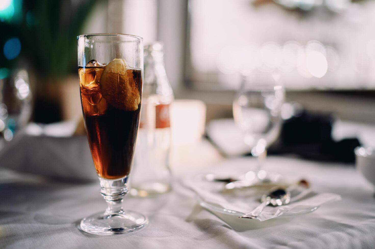 Vienna, Austria - July 14, 2024. Glass of cola with ice stands on a set table next to an empty bottle photo