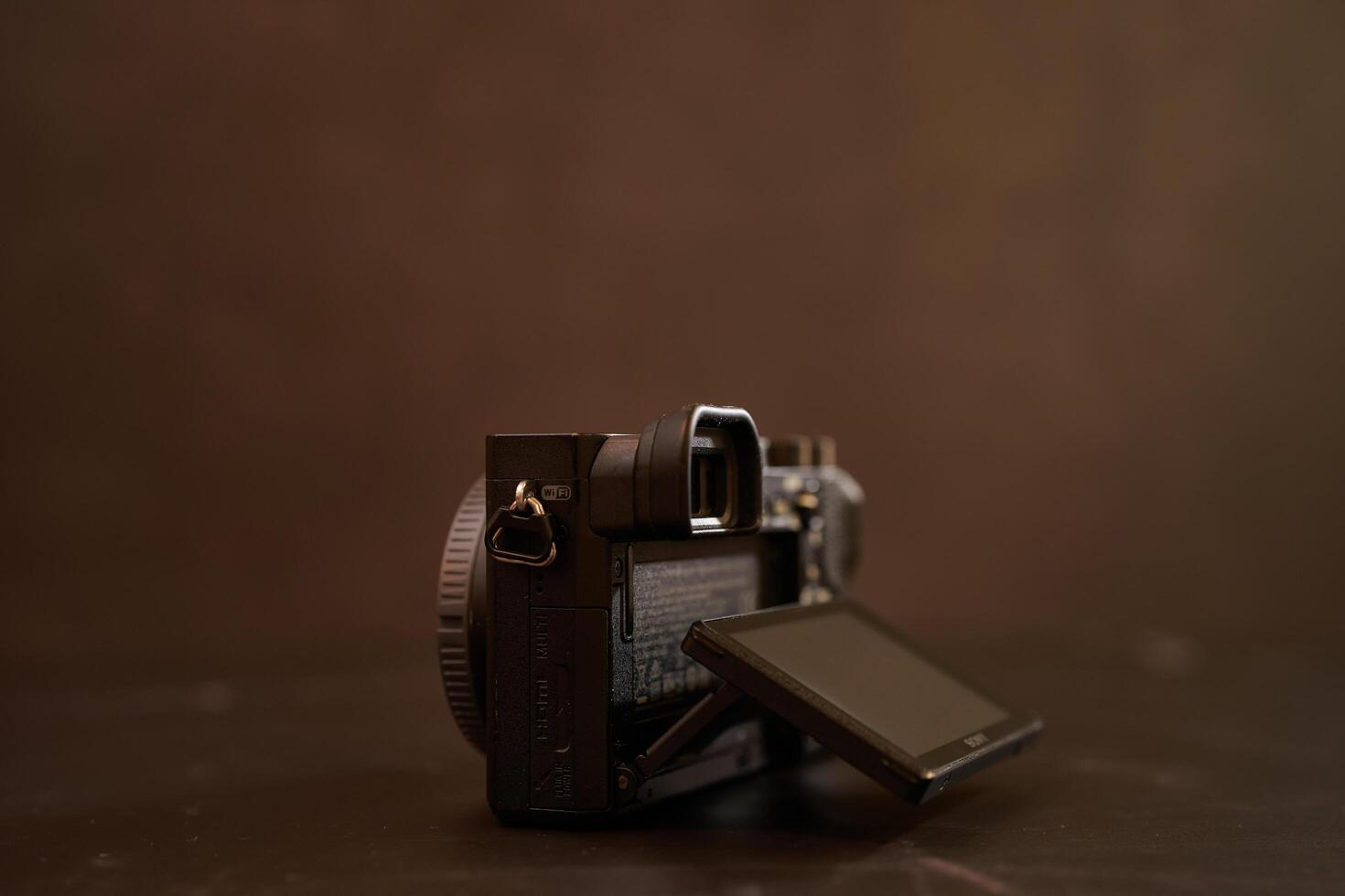 USA, Arizona - March 10, 2025. Sony A6000 mirrorless camera with its LCD display extended sits on a black table. Side view photo