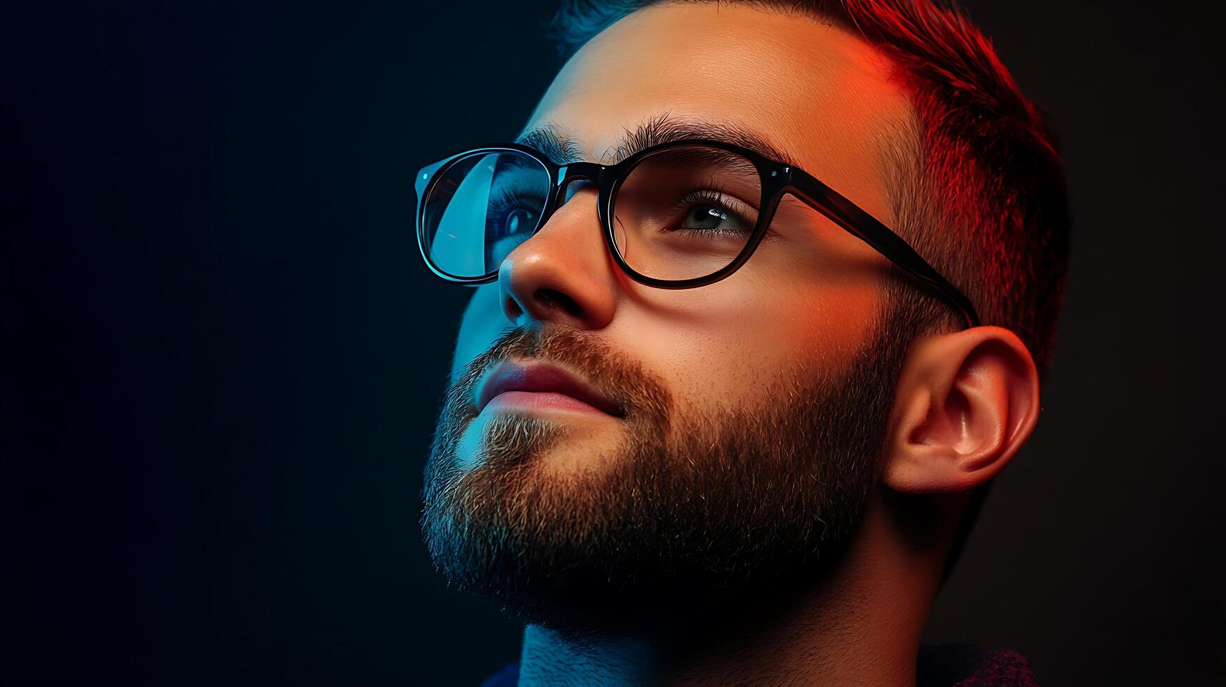 Stylish portrait of a thoughtful man with a beard and glasses looking upwards in vibrant blue and red studio lighting photo