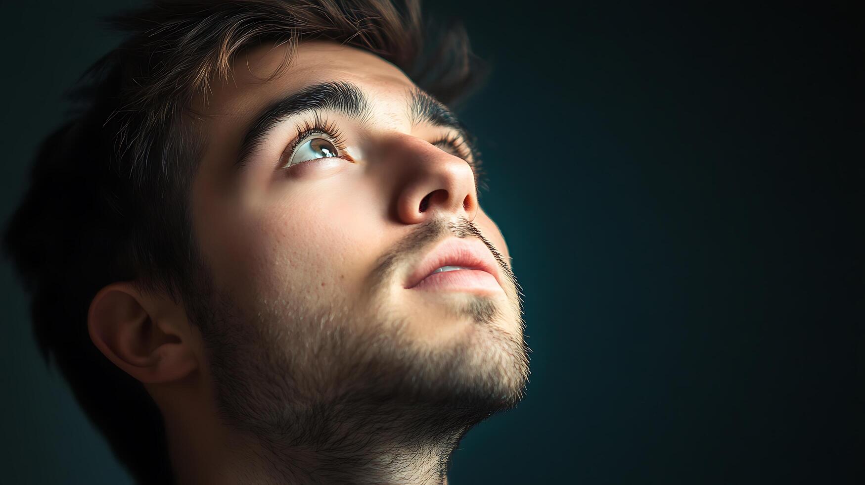 A young man with brown hair and eyes looking upwards A portrait against a dark background illuminated by soft light photo