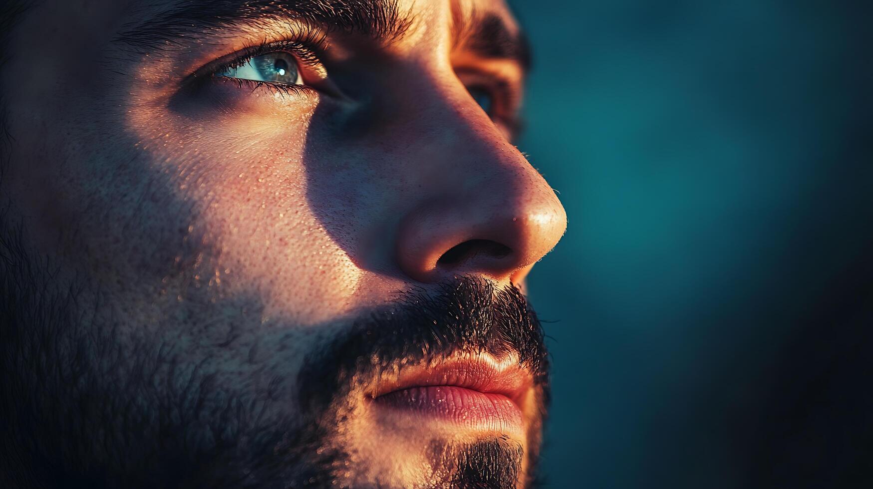 Contemplative portrait of a man illuminated by golden light gazing upwards with striking blue eyes and a thoughtful expression photo
