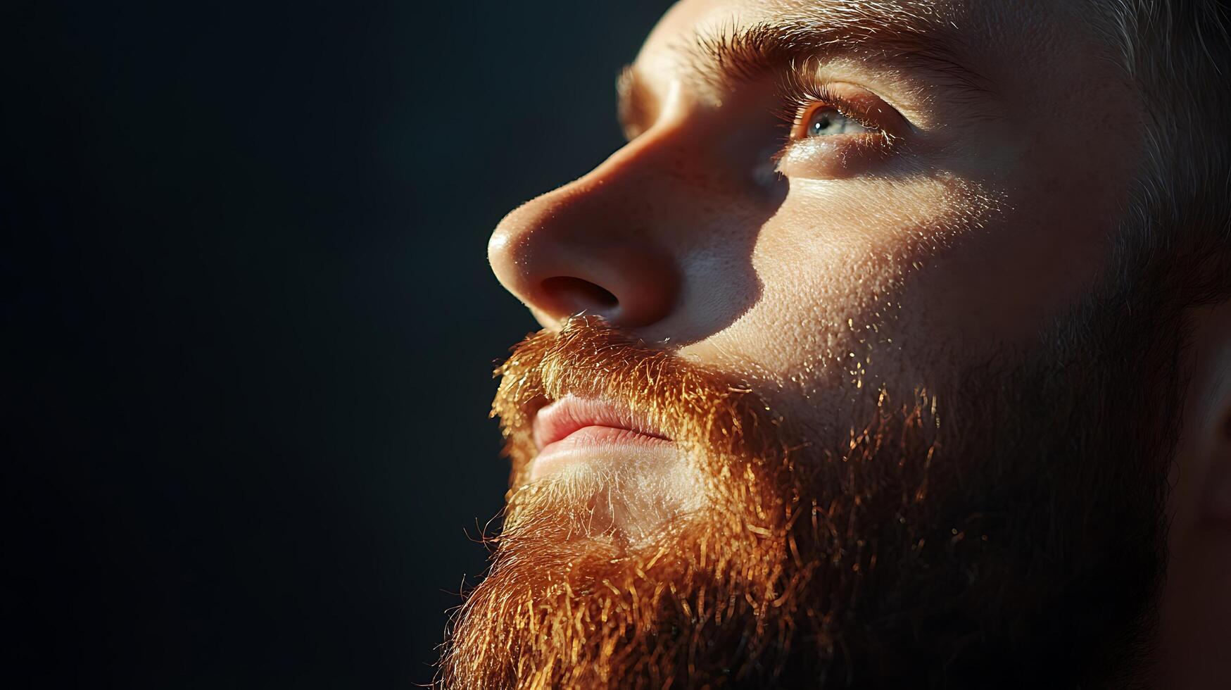 Contemplative portrait of a redhead man with a beard looking upward with light on his face against a dark background photo