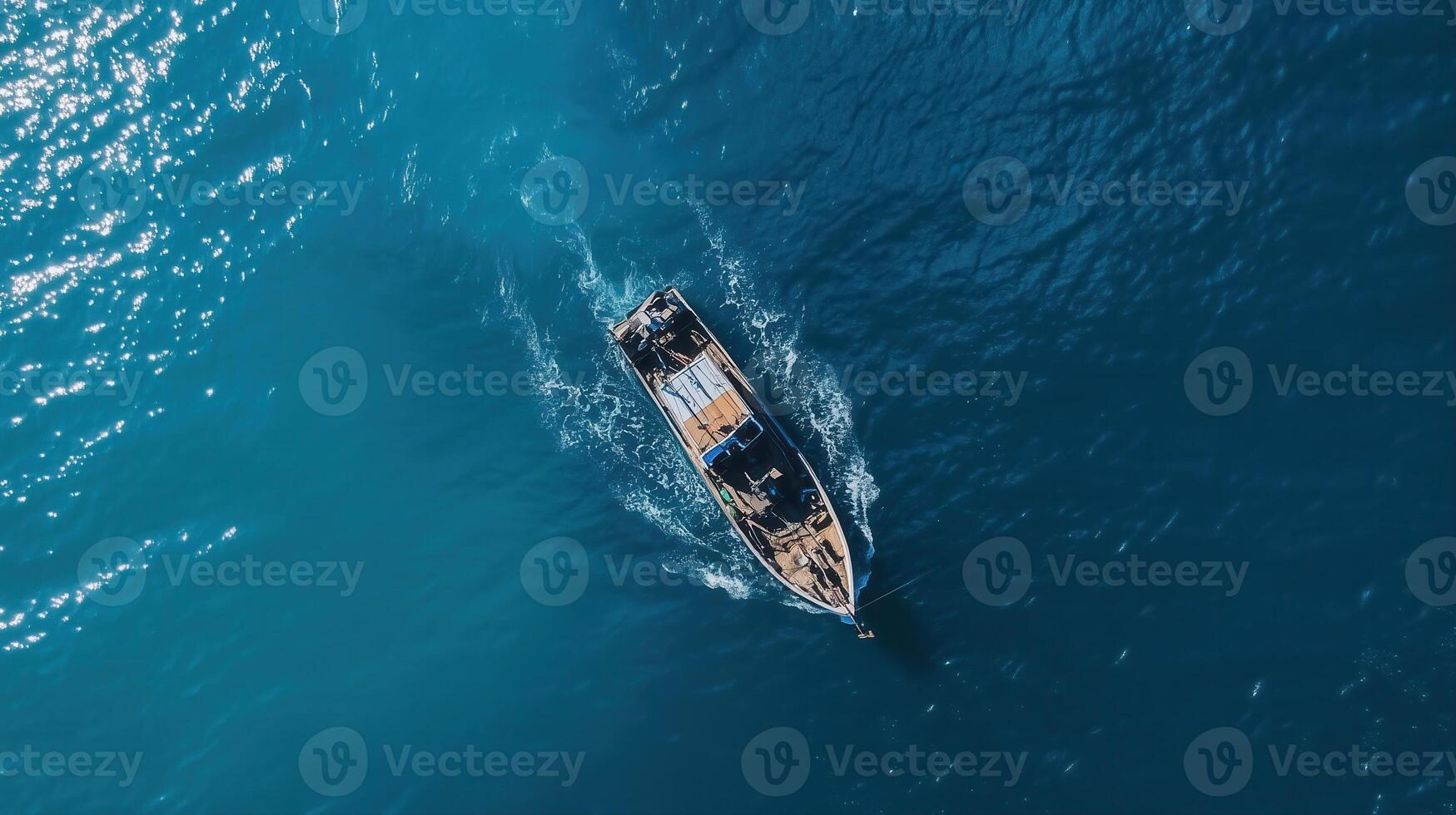 An aerial view shows a boat sailing on the deep blue water, creating a foamy wake behind it. photo