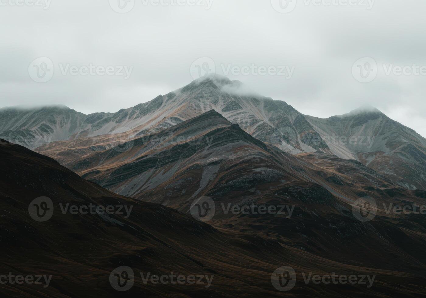 Layered mountains ascend into a cloudy sky, creating a dramatic and serene landscape view. photo
