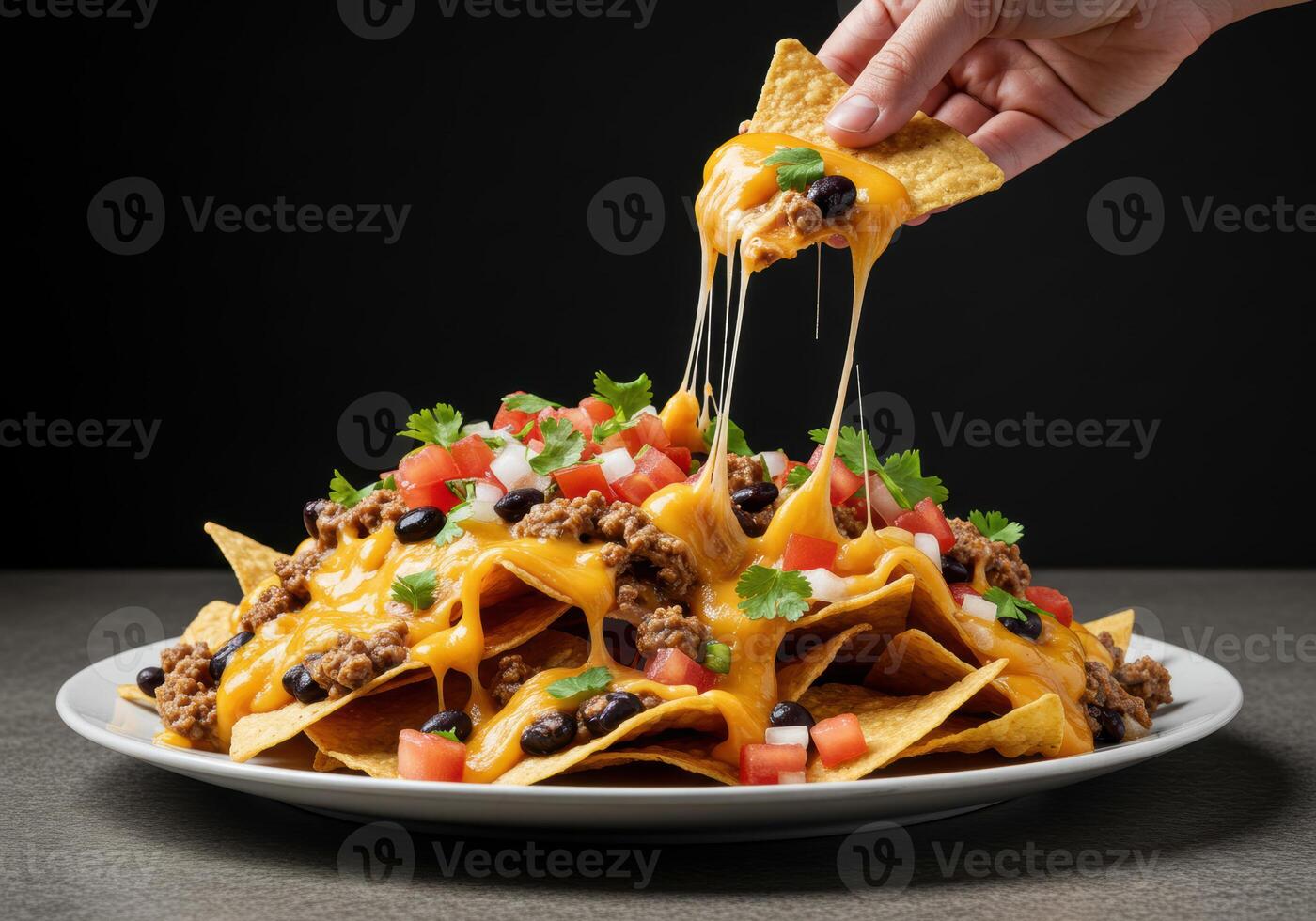 A hand pulls a cheesy nacho from a delicious plate of loaded tortilla chips with toppings. photo