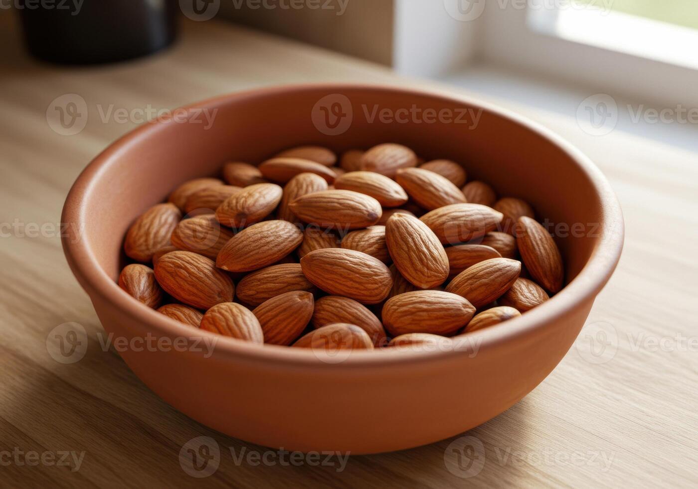 A bowl filled with delicious and nutritious almonds sits on a wooden table near a bright window. photo