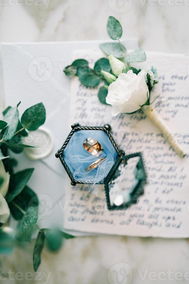 Wedding rings in a glass box lie on the oath next to the boutonniere photo