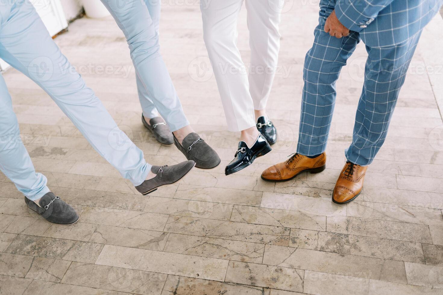 Groom and groomsmen show off their shoes with outstretched feet. Cropped. Faceless photo