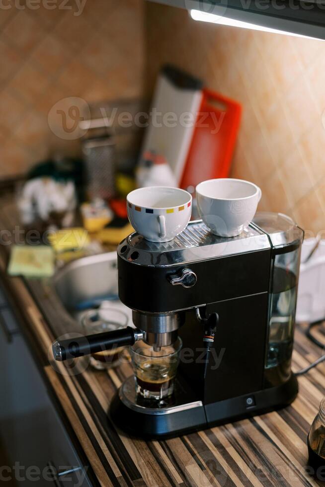 Cups with coffee stand on a carob coffee machine preparing coffee on the table photo