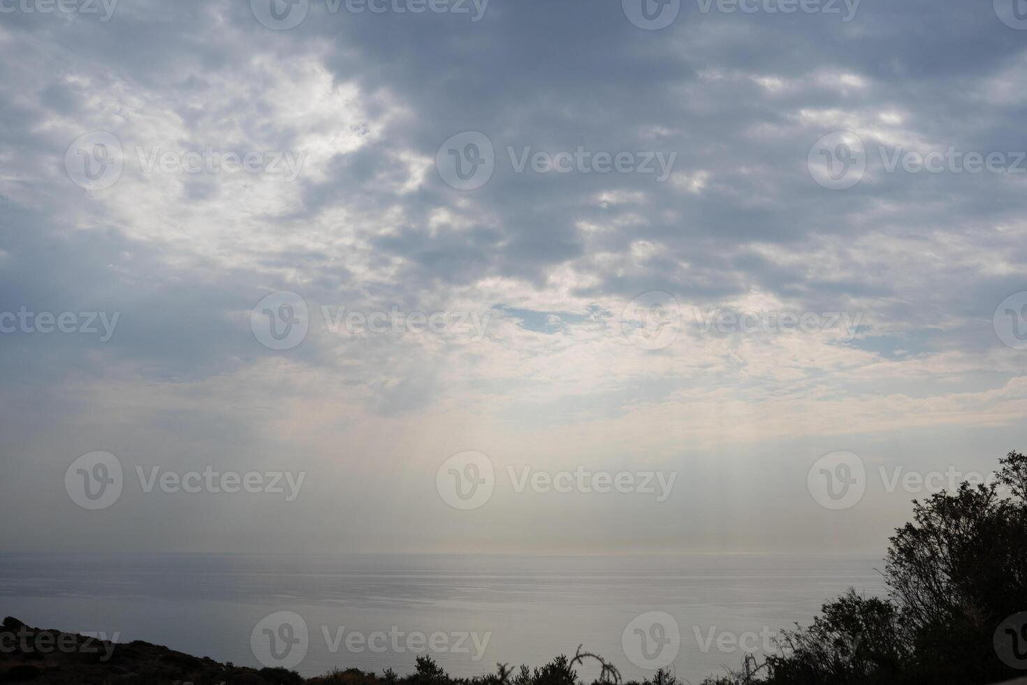 White and gray cloudy sky with sun rays called 'God's rays' above the sea photo
