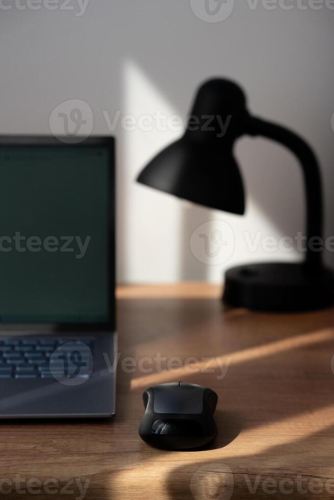 A minimal wooden table top scene of laptop with blank screen, and lamp behind. Modern workplace. Cozy space. photo