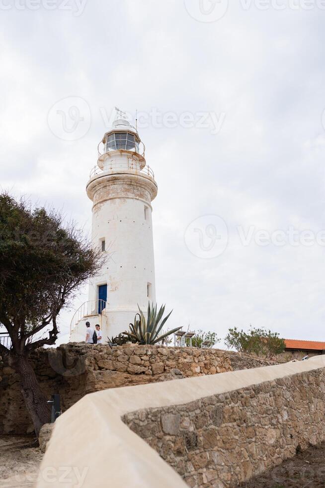 White lighthouse s under a partly cloudy sky flanked by trees photo