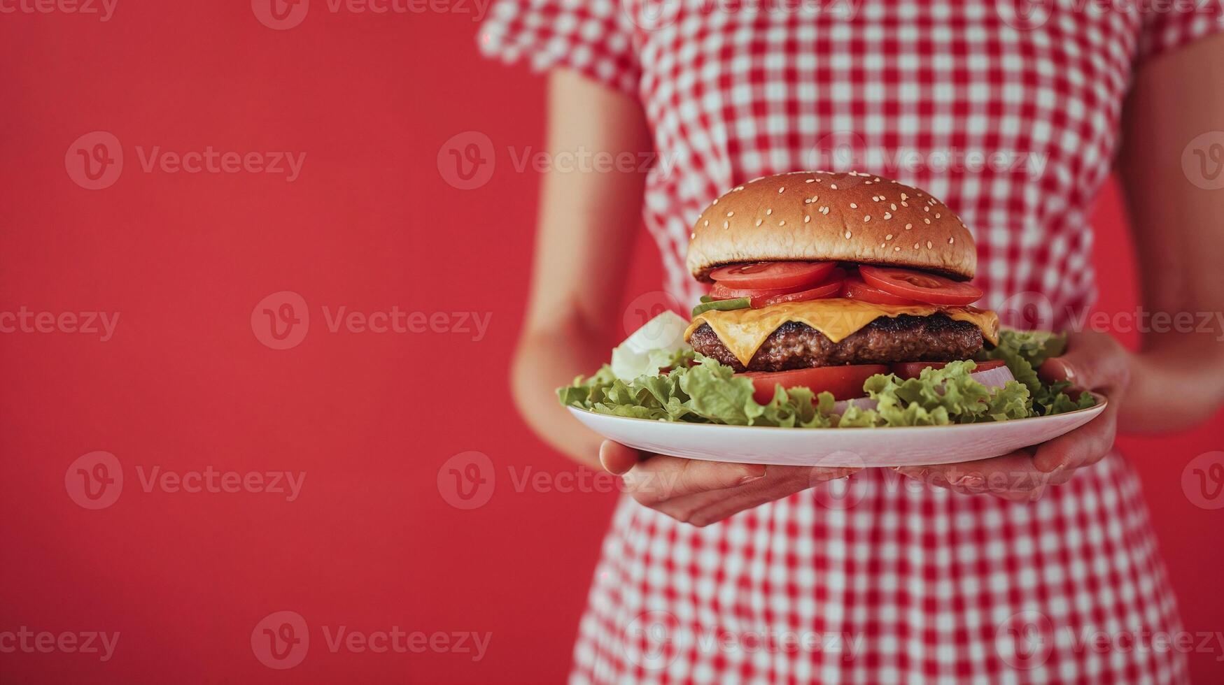 Close-up of a cheeseburger on a plate, held by a person in red gingham, vibrant red background, fresh look. photo