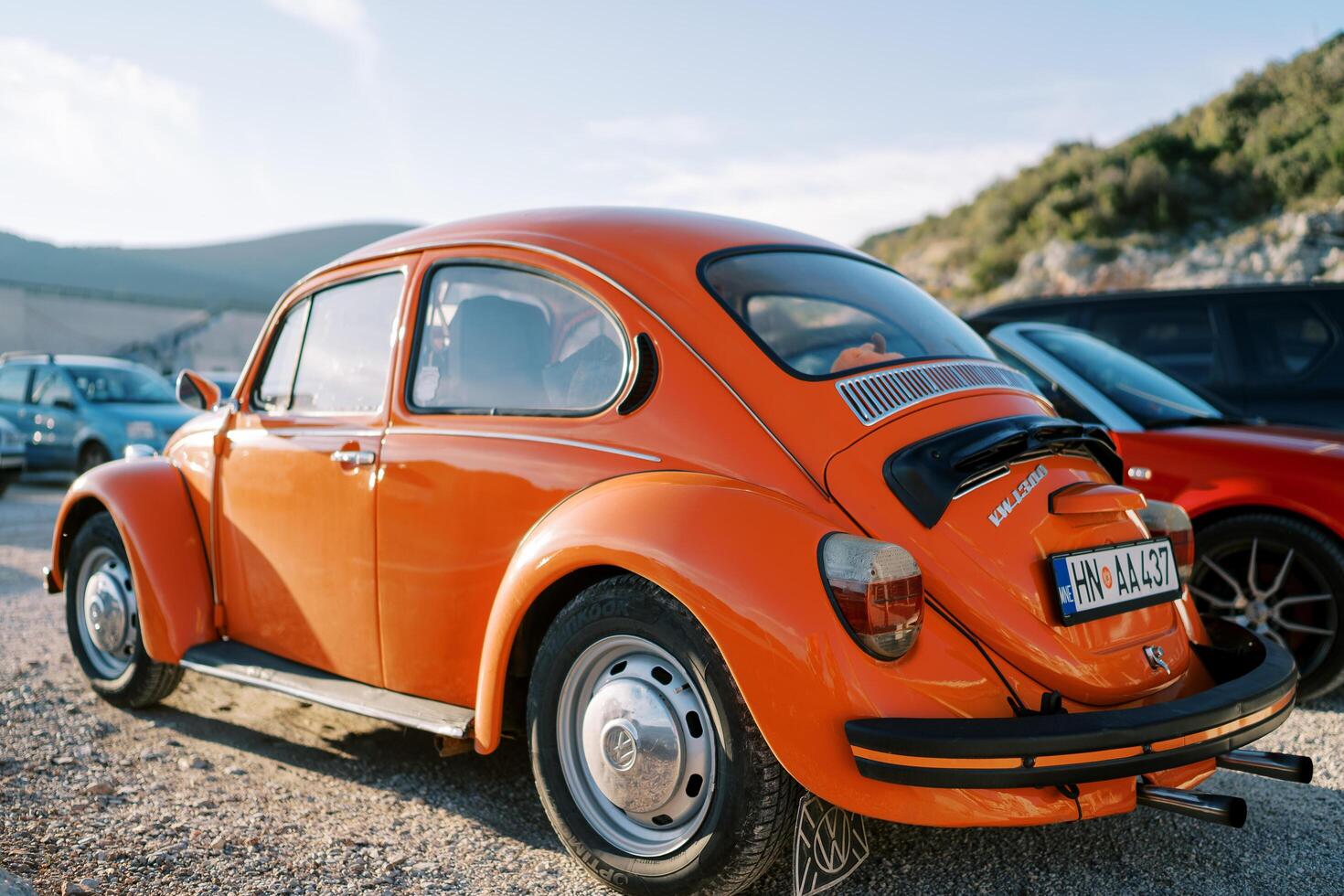Montenegro, Budva - March 04, 2022. Orange Volkswagen beetle stands in a parking lot near the mountains. Back view photo