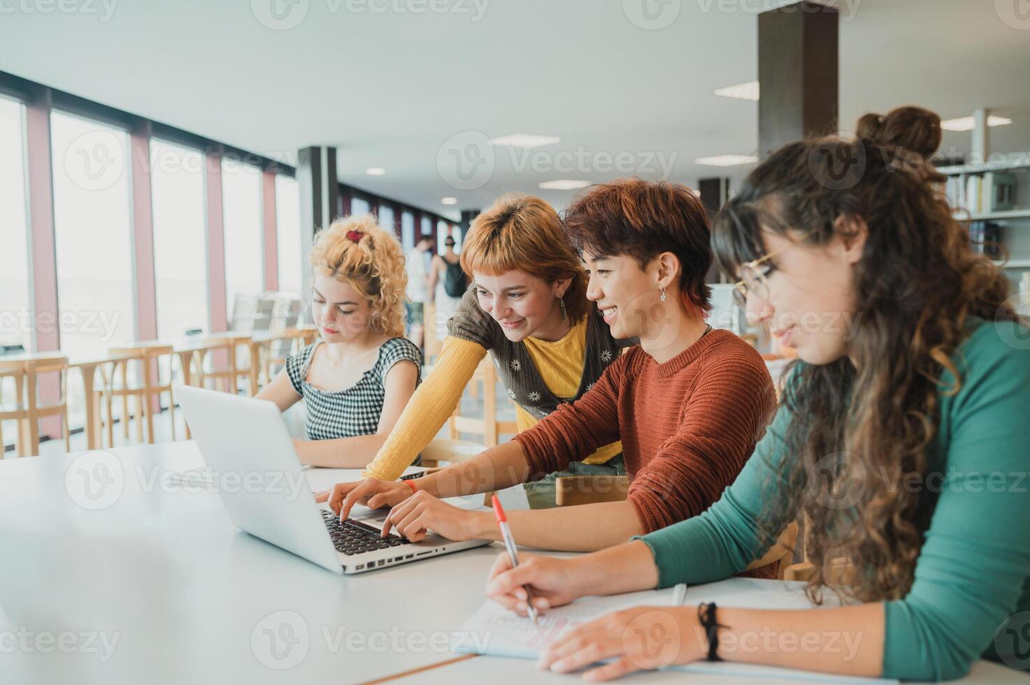 Four young people working on a laptop in a library photo