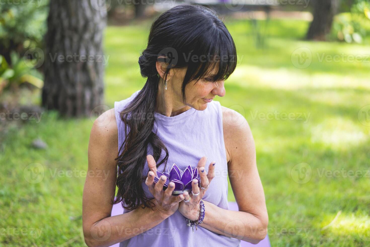 A woman is sitting on the grass holding a purple flower photo