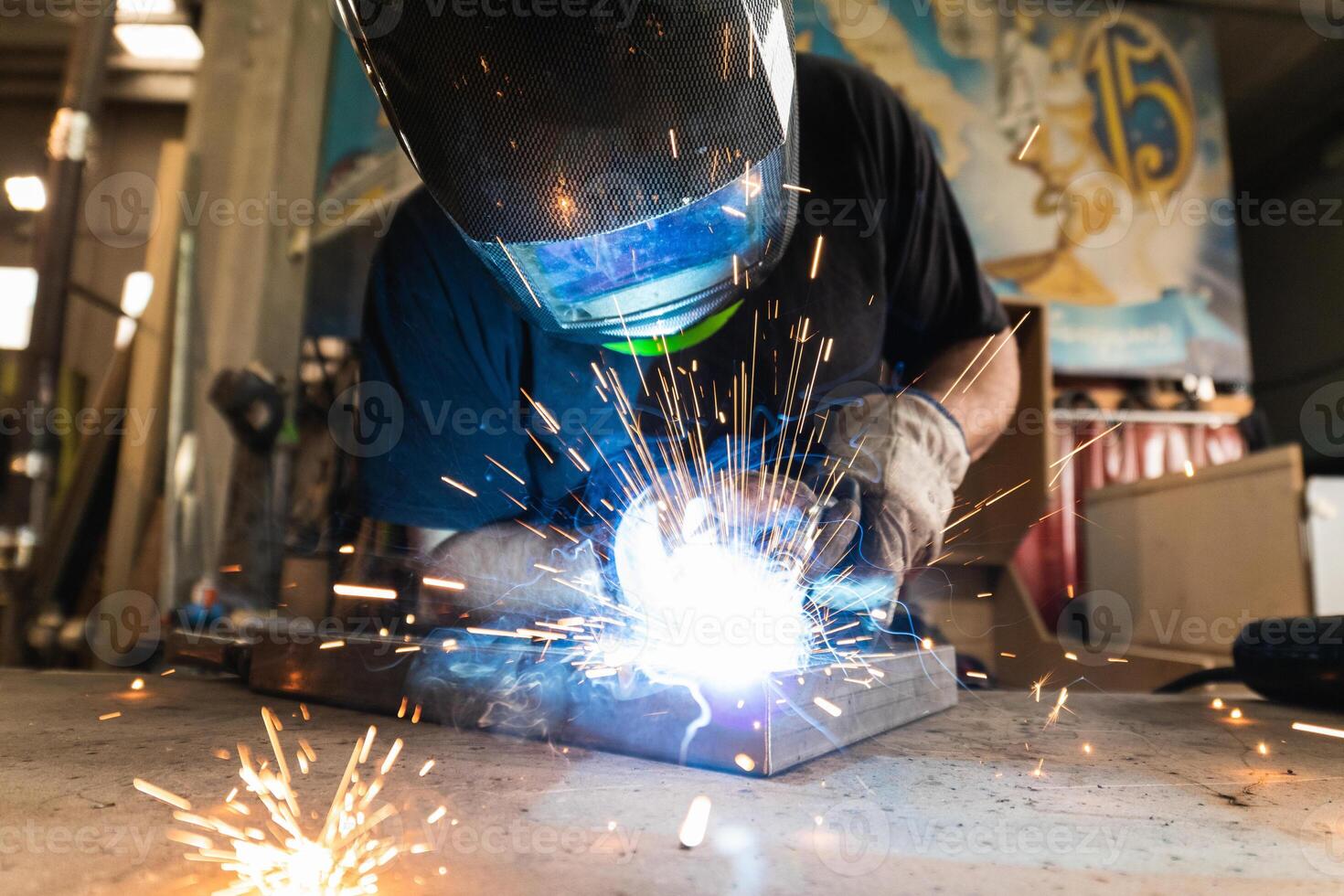 Welder in protective helmet welding metal detail in workshop photo