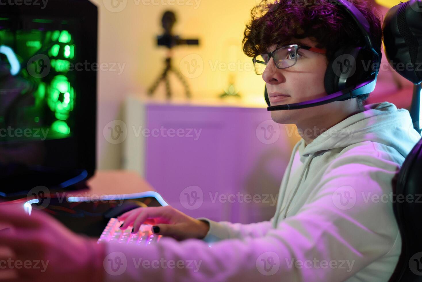 Young man in headphones playing on keyboard and sitting at table with gadgets photo