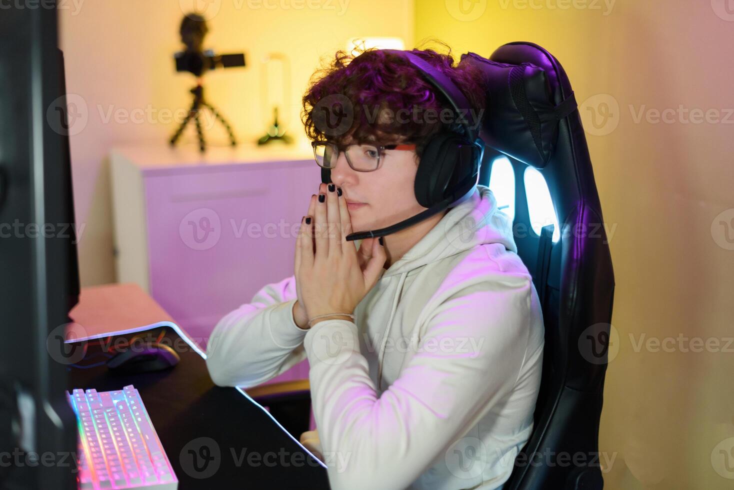Young man in headphones playing on keyboard and sitting at table with gadgets photo