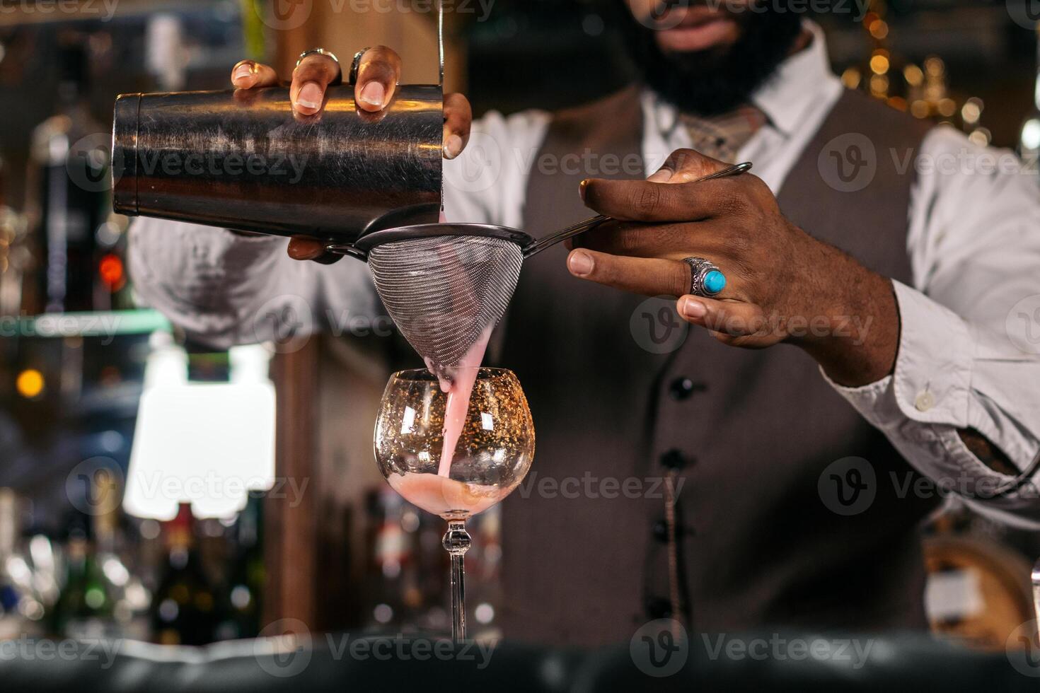Close-up of the hands of a stylish black bartender preparing a cocktail in a shaker in a traditional cocktail bar photo