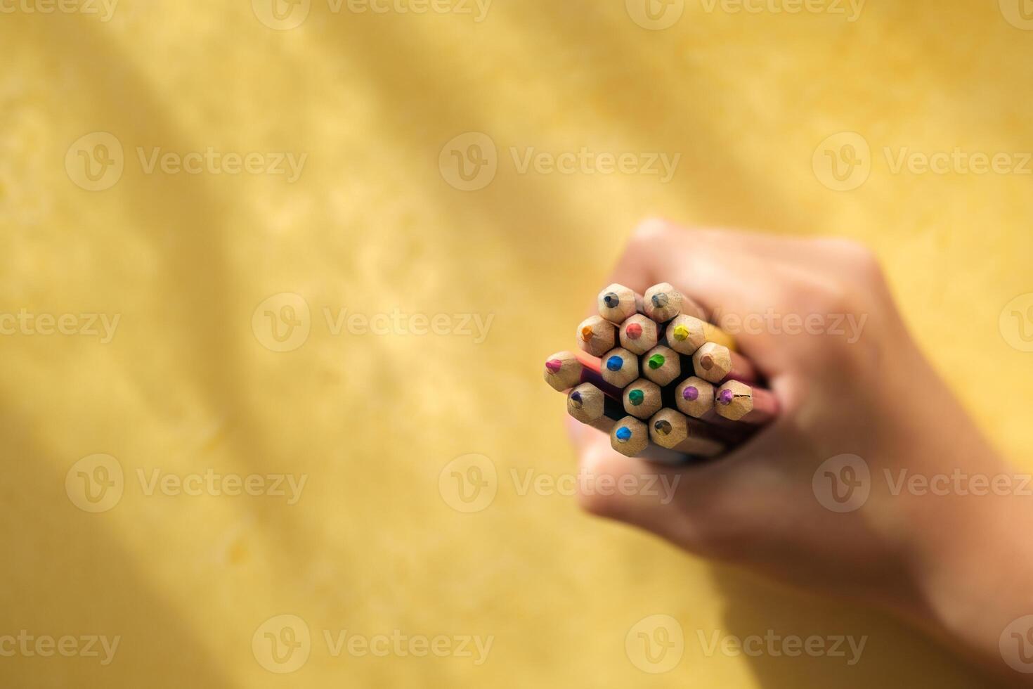 A child's hand picking up coloured pencils on a yellow backgroun photo