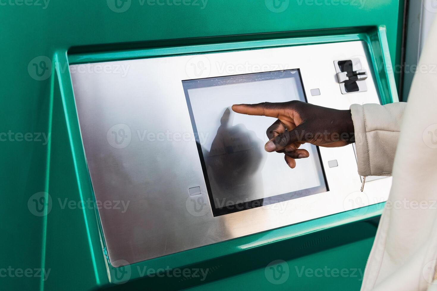 Anonymous black businessman touching screen of ATM in town photo