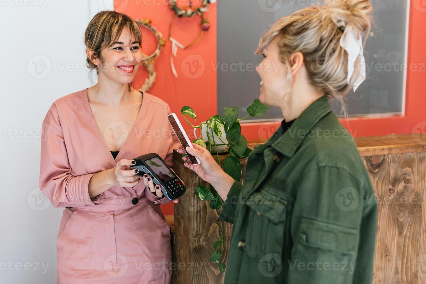 Delighted woman paying for skin care treatment with smartphone on POS terminal photo