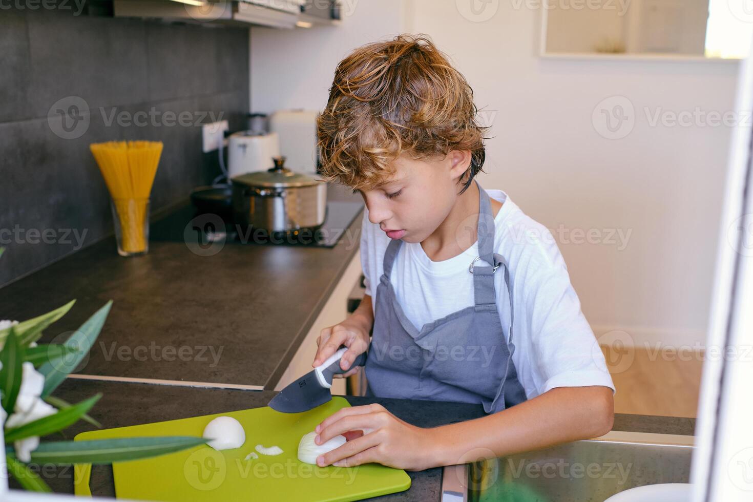 Focused boy cutting fresh onion while cooking in kitchen photo