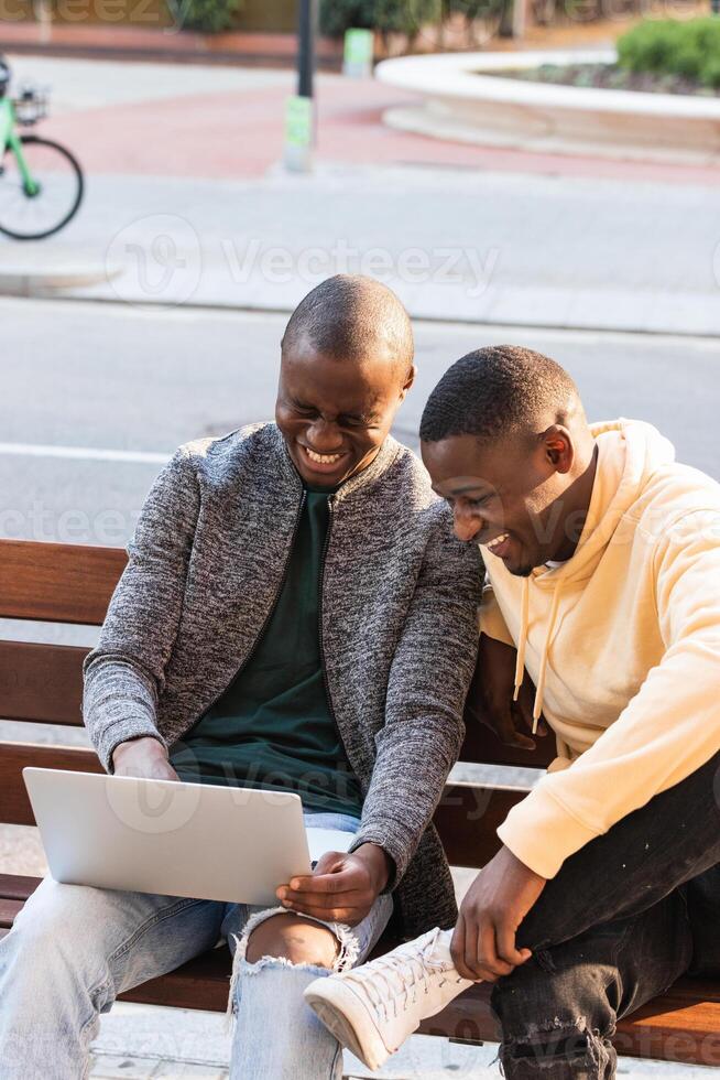 Smiling black men using laptop while sitting on bench photo
