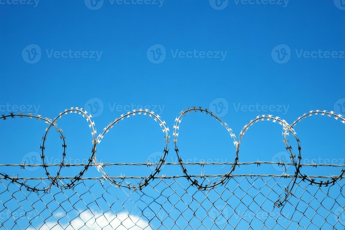 Razor wire forming protecting circles on top of chain link fence under blue sky photo