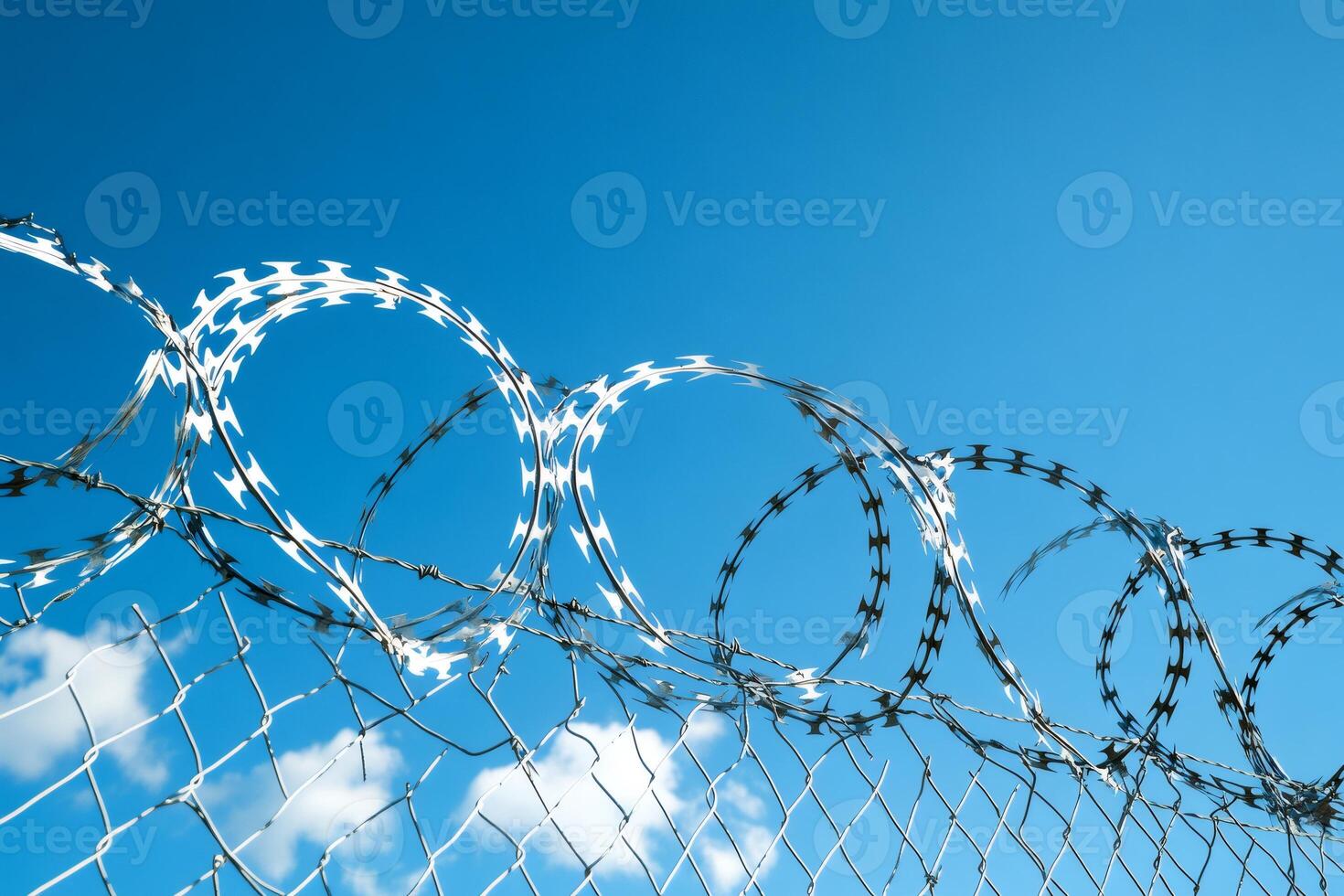 Razor wire coils protecting a perimeter fence under blue sky photo