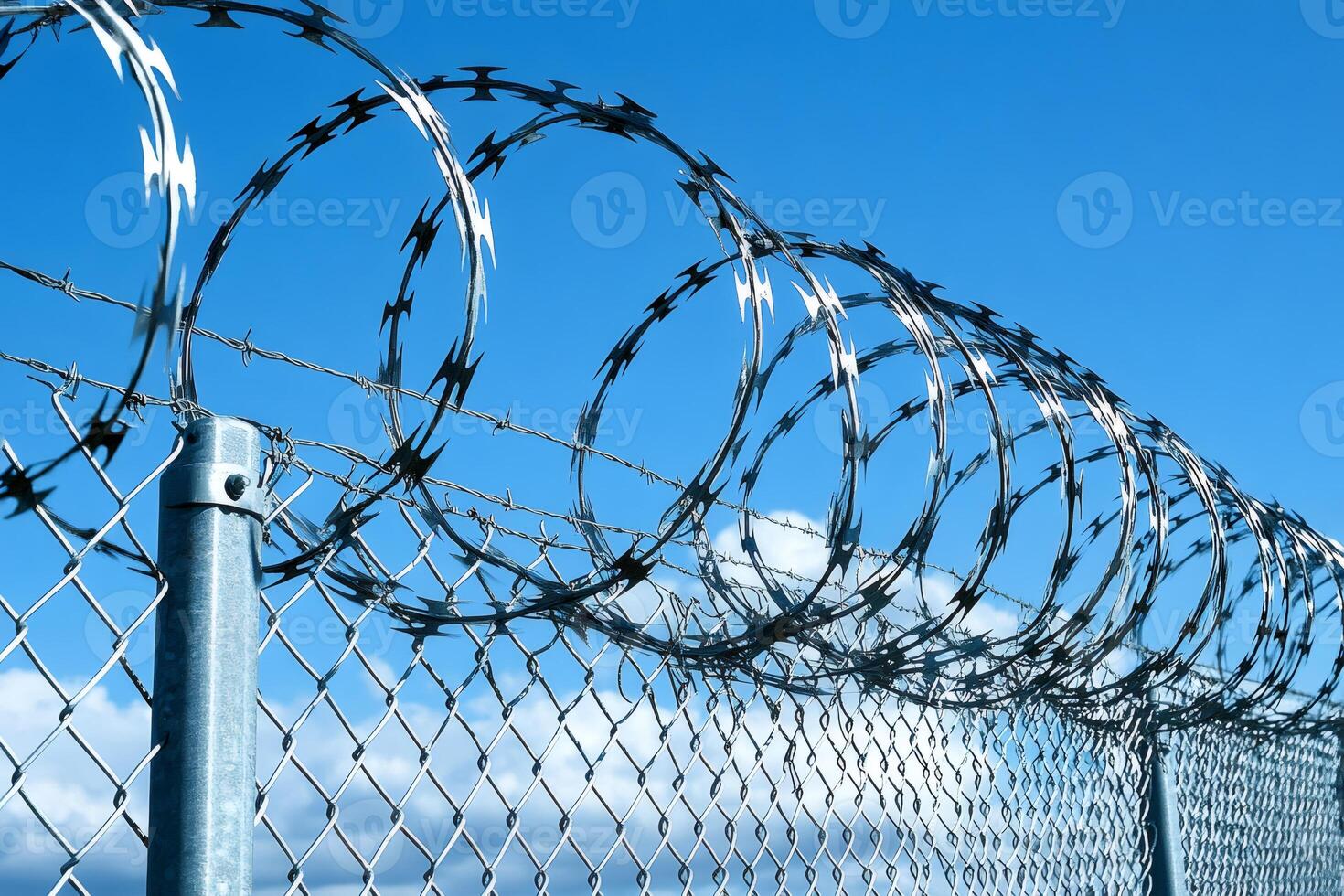 Razor wire coils protecting chain link fence under blue sky photo