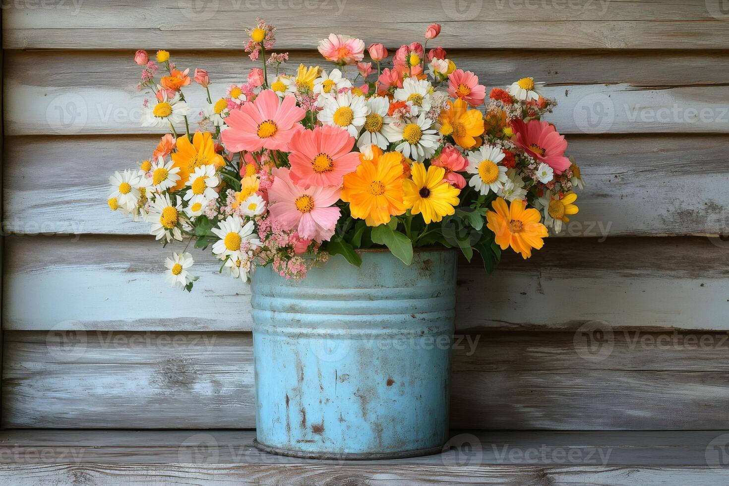 Colorful summer flowers blooming in rustic blue metal bucket on wooden shelf photo