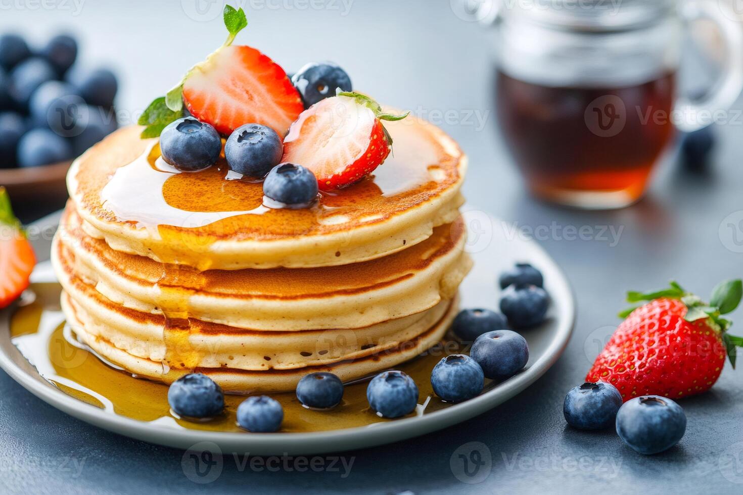 Stack of pancakes dripping with syrup topped with fresh strawberries and blueberries photo