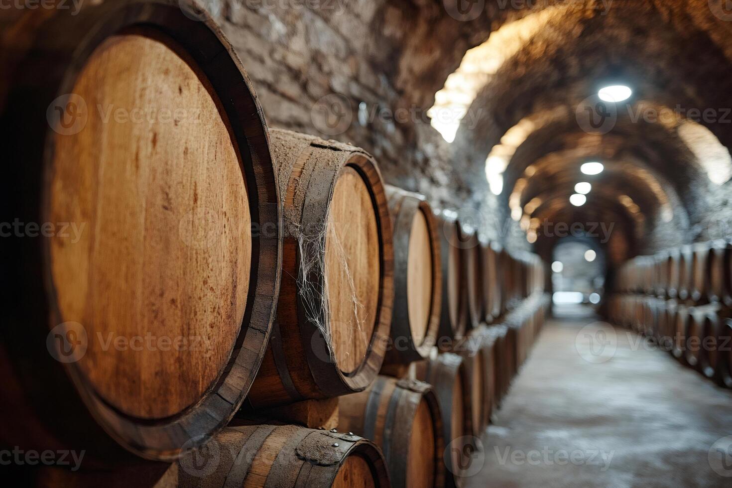 Wine barrels stacked inside a winery cellar creating a long tunnel with stone walls photo