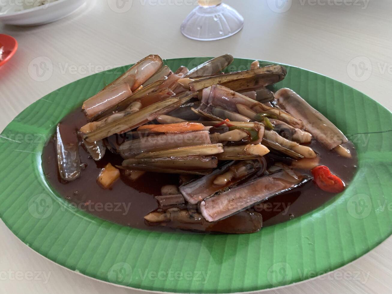 A Chinese Dish Bamboo clams steamed in sweet and sour sauce garnished with Spring Onions and Fried Garlic on green plate 1 photo