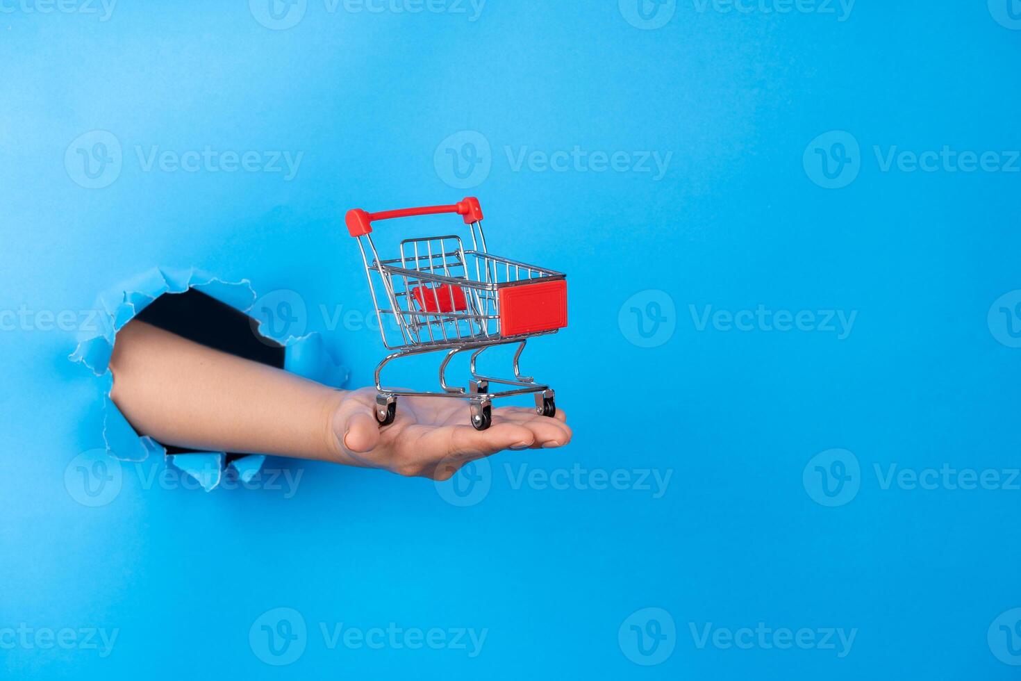Female hand holding shopping cart from blue torn pape photo