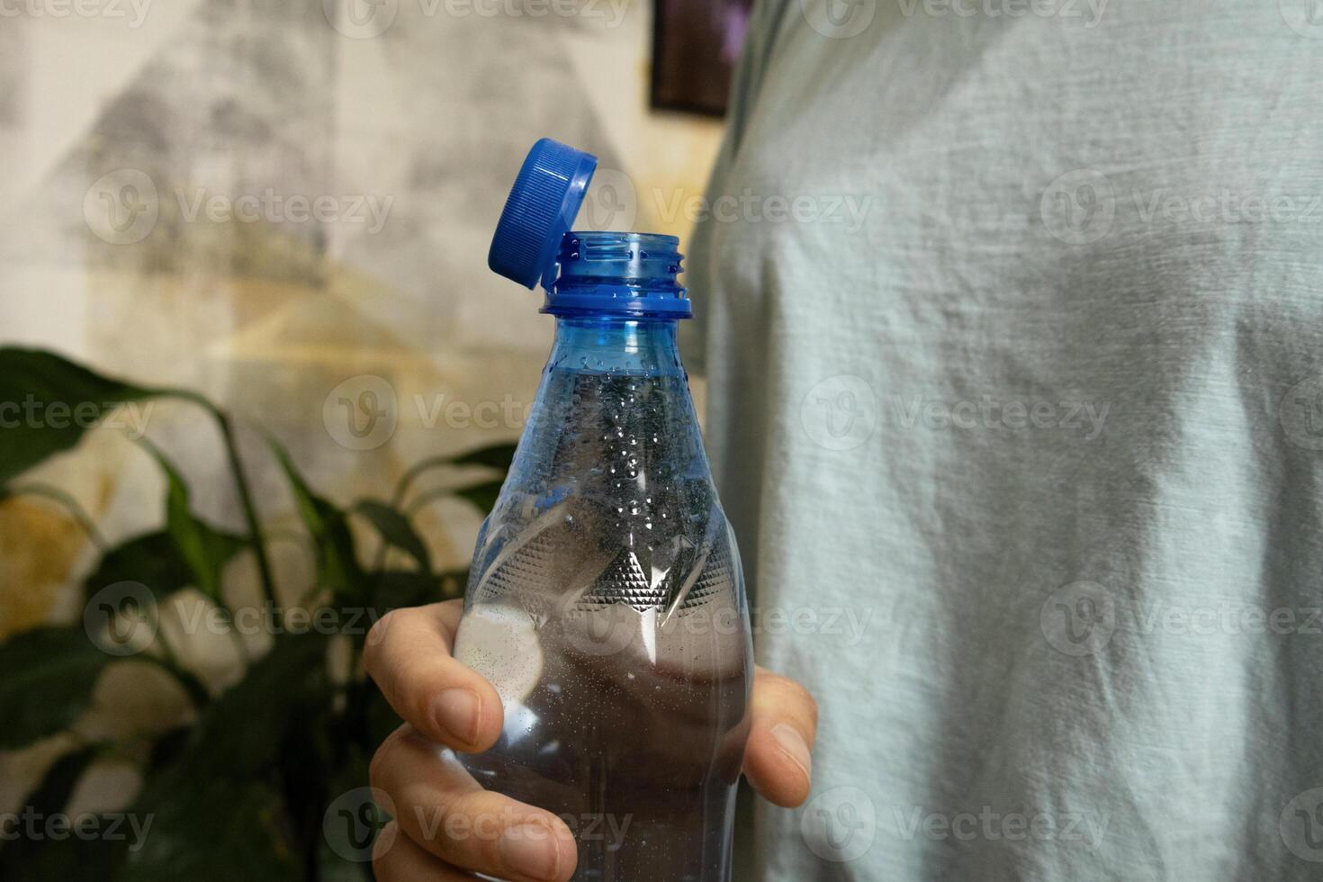 Bottle with stationary plastic cap in woman hand. Green plants in background photo