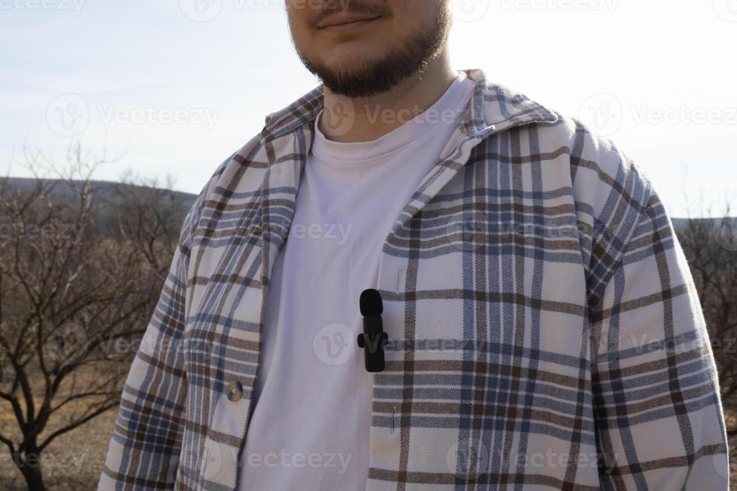 A small buttonhole microphone on a man's shirt. The man fixed the mini microphone to his shirt photo