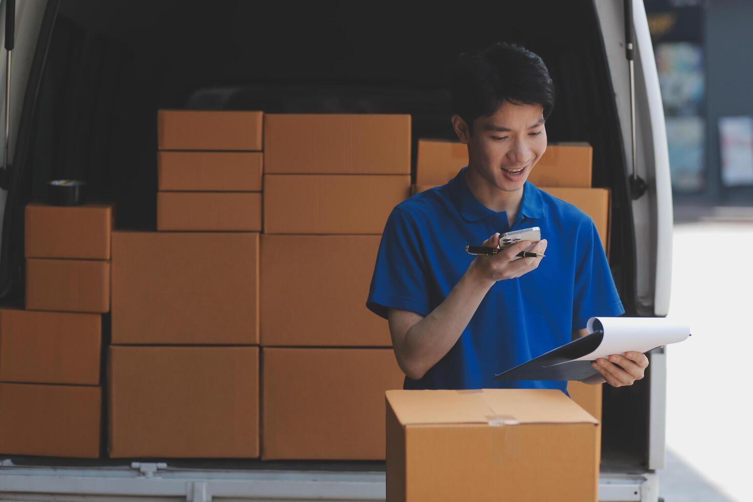 A young man in a blue shirt is standing in front of a van with boxes photo