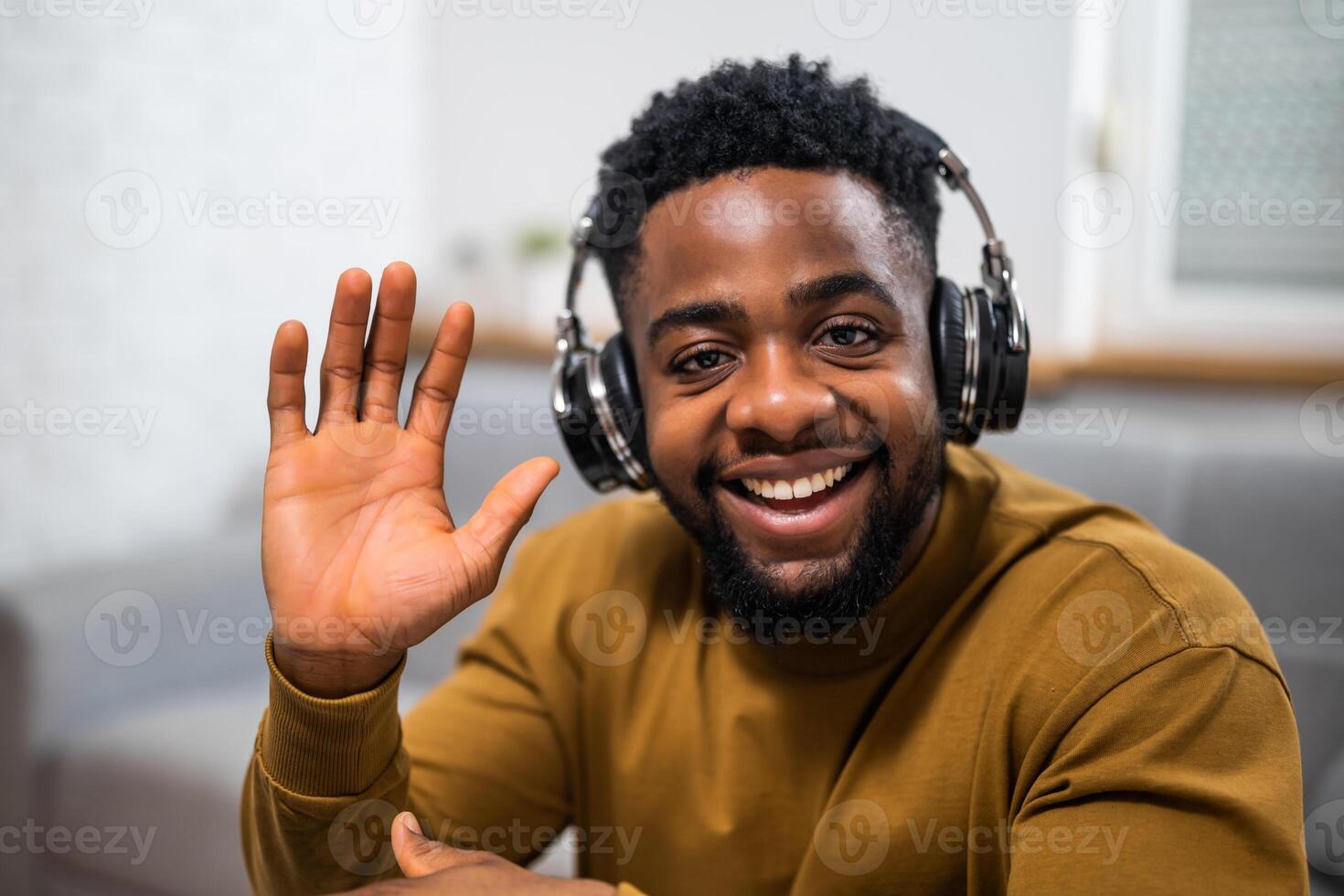 Close up portrait of smiling young African American man looking at camera and waving during a call on his laptop while sitting in his comfortable home. photo