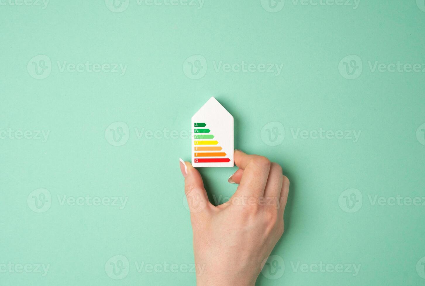 Hand holding a figurine of a house with an energy efficiency rating scale. Optimizing energy use. Cost savings, environmental responsibility, and energy conservation. photo