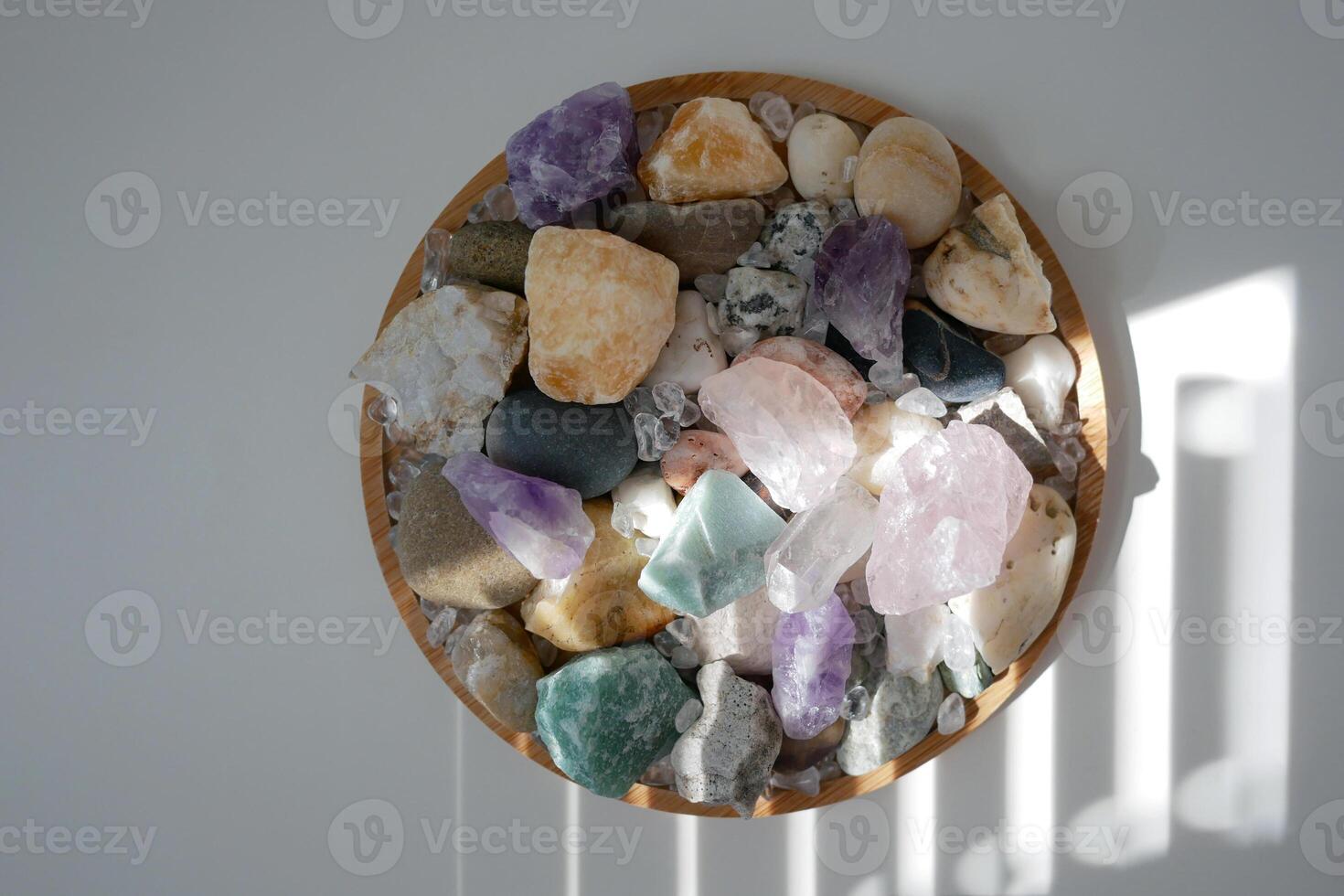 Stones, minerals, crystal, pebble on a round stand on a white background with shadow and light from blinds. the concept of interior details or esoteric rituals and meditation photo