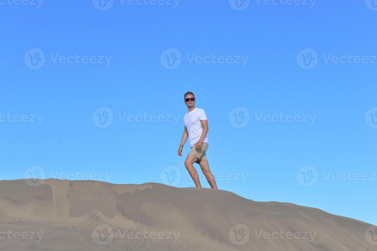 A young man walking along a sand dune through barkhan in Maspalomas, Gran Canaria on a hot day. A self confident man goes up the mountain - success and achievements concept photo