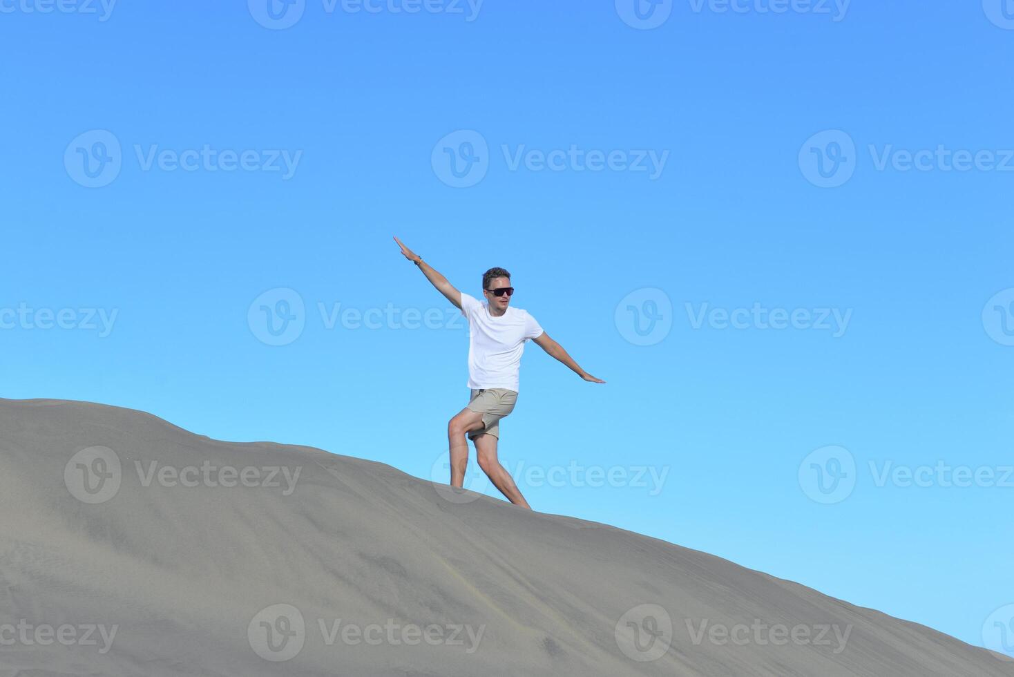 A man walking along a sand dune through barkhan in Maspalomas, Gran Canaria on a hot sunny day. A self confident man goes up the mountain - success and achievements concept photo