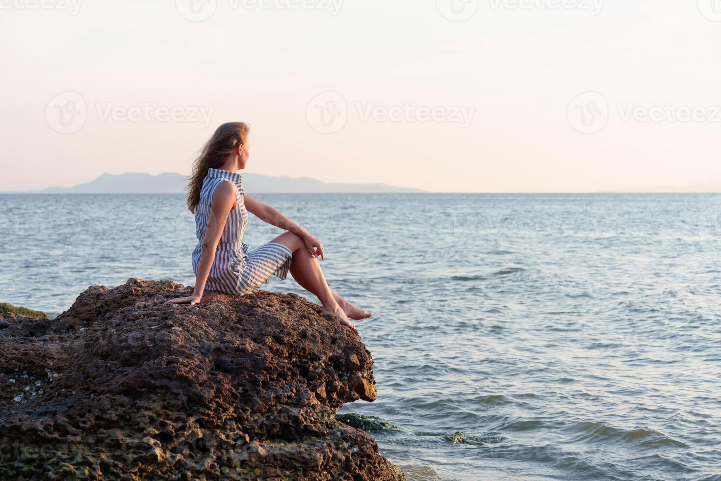 Woman relaxing on rock contemplating inspiring ocean view at sunset photo