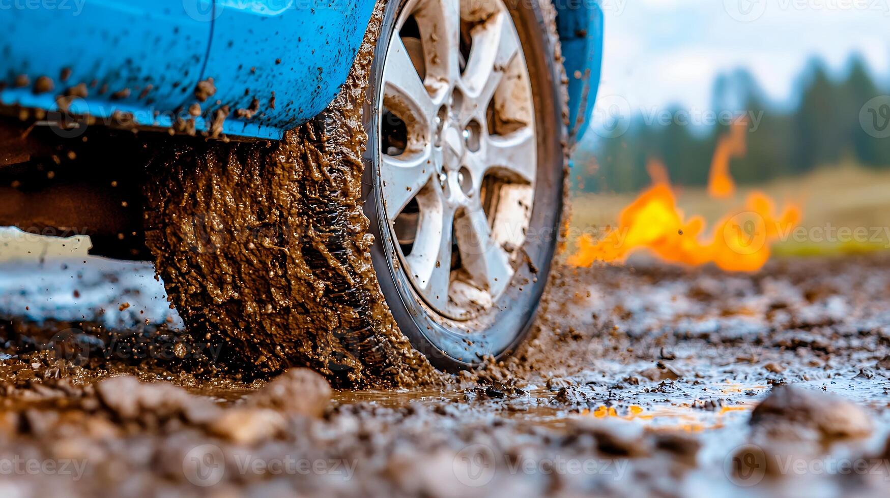 Blue Car Wheel Splashing Mud with Fire in Background Under Dramatic Sky photo