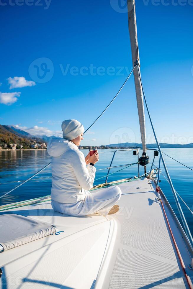 Woman hands holding thermo mug sitting on bow of the yacht during sailing in the morning in winter in Adriatic sea, relaxation in yachting time photo