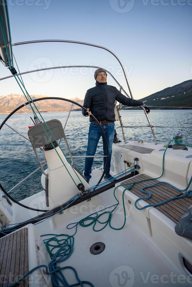 Young man captain standing at helm and controls a sailboat during a journey by sea in winter time in Montenegro photo