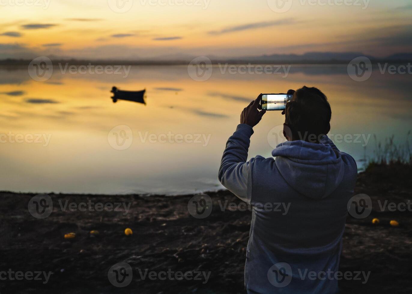 Male silhouette taking photo of boat at sunset